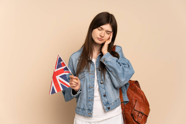 Ukraynalı genç bir kız, bej arka planda başağrısı ile izole edilmiş bir Birleşik Krallık bayrağı tutuyor. - Fotoğraf, Görsel