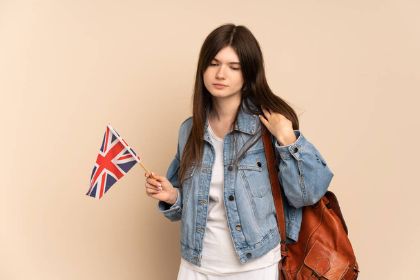Ukraynalı genç bir kız, bej arka planda izole edilmiş bir Birleşik Krallık bayrağı taşıyor. - Fotoğraf, Görsel