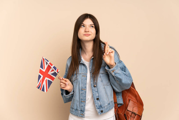 Ukraynalı genç bir kız bej arka planda izole edilmiş bir Birleşik Krallık bayrağı tutuyor. - Fotoğraf, Görsel