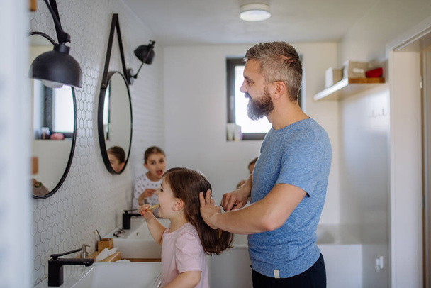 Padre spazzolando i suoi piccoli capelli figlie in bagno, concetto di routine del mattino. - Foto, immagini