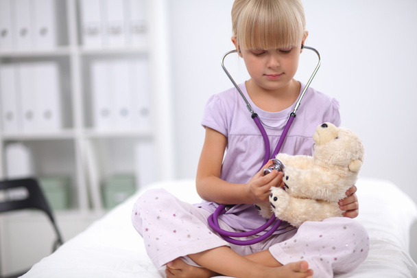 Little girl is examining her teddy bear using stethoscope - Фото, изображение