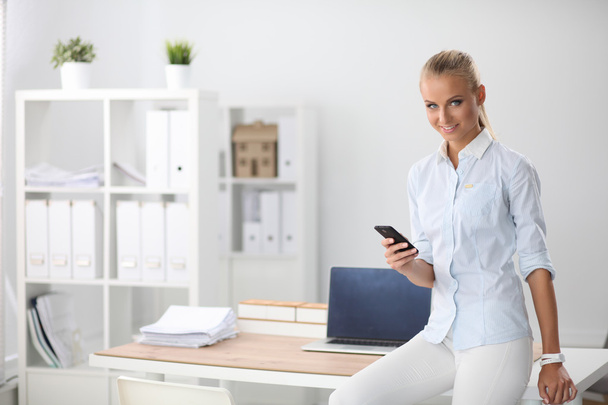 Bizneswoman wysyłanie wiadomości ze smartfonem siedzi w biurze - Zdjęcie, obraz