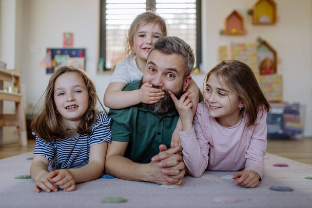 Cheerful father with three little daughters lying on floor together at home. - Photo, Image