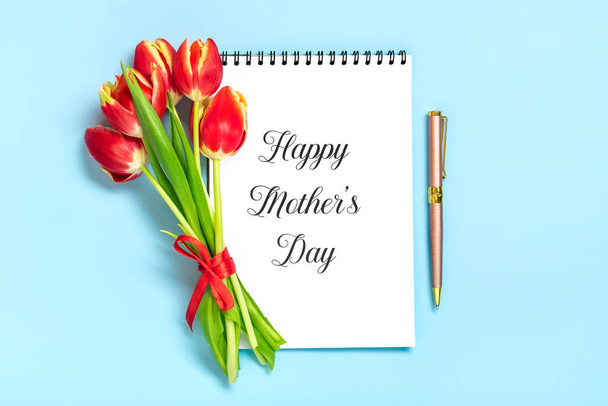 Bouquet of red tulips, text Happy Mothers Day on open white notepad on blue background Top view Flat lay Holiday greeting card - Photo, Image