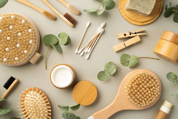Top view photo of spa accessories anti-cellulite washcloth hair brush cream bottle tube soap on wooden stand cotton buds toothbrushes clothespins and eucalyptus on isolated pastel grey background - Foto, Imagem