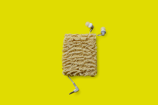 tangled headphone wires. concept photo. instant noodles and headphones isolated on yellow background. - Fotografie, Obrázek