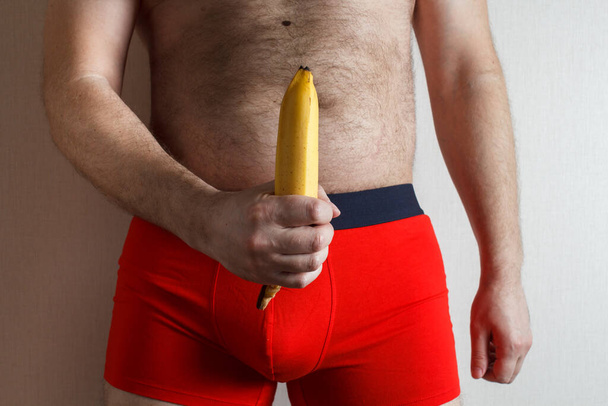 young handsome man in red shorts. banana in the hands symbolizes a large penis. - Fotó, kép
