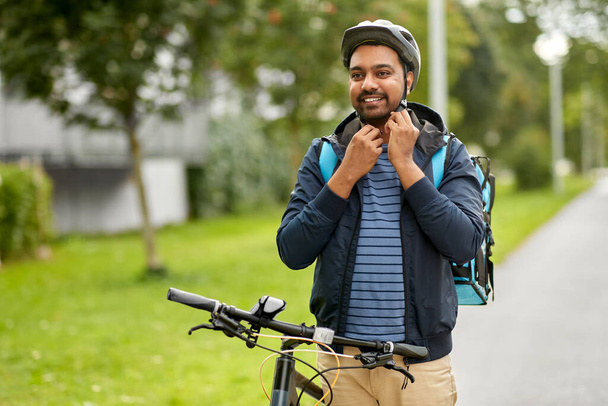 food delivery man fastening bicycle helmet in city - Φωτογραφία, εικόνα