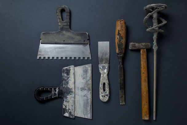 plasterer's tool in plaster. set of dirty tools for plastering work. Flat lay tools. Spatula, hammer, whisk and chisel lie on the concrete. - 写真・画像