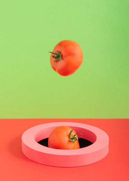 Οι ντομάτες πέφτουν στην τρύπα μέσα από ένα ροζ δαχτυλίδι σε πράσινο και κόκκινο φόντο - Φωτογραφία, εικόνα