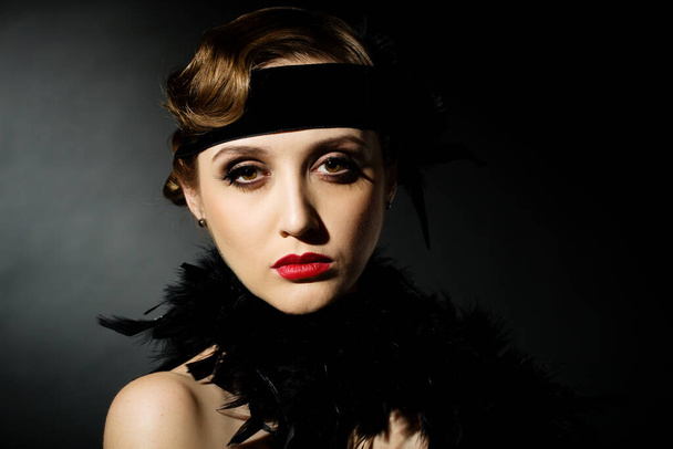 Porträt eines glamourösen dunkelhaarigen Models mit perfektem Make-up, das eine luxuriöse Halskette, einen schwarzen Body und ein langes Oberteil trägt, die Hände hinter dem Kopf hält und geradeaus blickt. - Foto, Bild