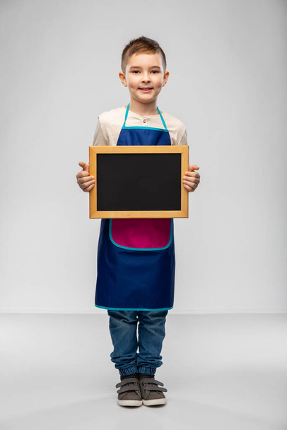 smiling little boy in apron holding chalkboard - Foto, Imagen