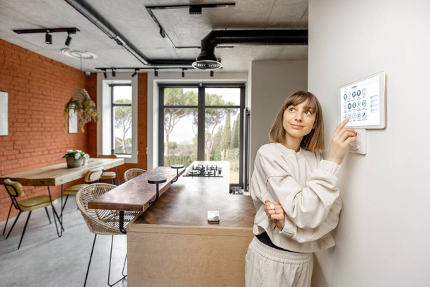 Woman controlling home devices with digital smart panel mounted on the wall - Foto, Bild