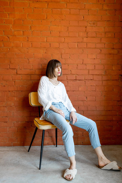 Portrait of a woman on chair on brick wall background - Φωτογραφία, εικόνα