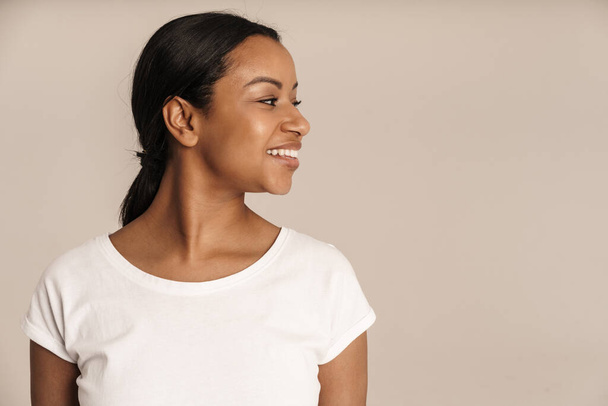 Joven mujer negra vistiendo camiseta sonriendo y mirando a un lado aislado sobre la pared blanca - Foto, Imagen