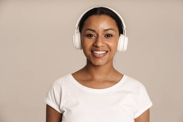 Young black woman smiling while listening music with headphones isolated over white wall - Foto, afbeelding