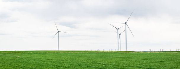 Tuulivoimapuiston kolmen tuulivoimalan ympäristömerkki tai otsikkokuva, joka tuottaa uusiutuvaa energiaa. Puhdas vihreä vaihtoehtoinen voima. Tuulienergia ilmastonmuutoksen ja ilmaston lämpenemisen torjunnassa. - Valokuva, kuva
