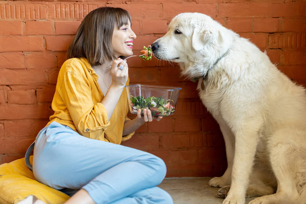 woman feeding her cute dog with salad indoors - Photo, Image