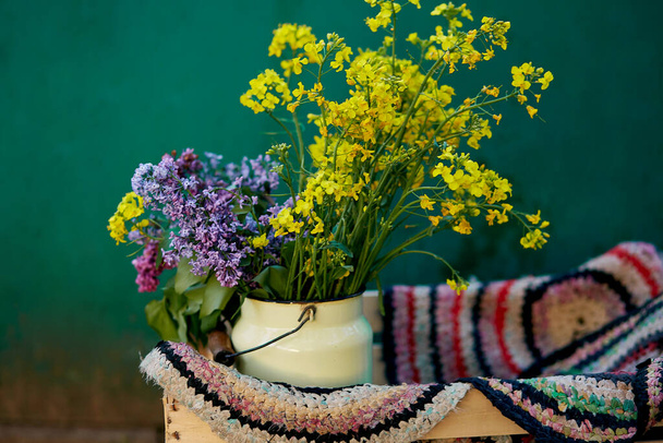 Vintage colorful handmade rug and spring flowers in watering can. Country life,cottage core, creative rustic patchwork concept. Copy space - Fotografie, Obrázek