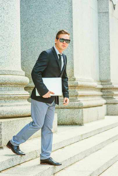Businessman working in New York. Dressing in black blazer, tie, gray pants, leather shoes, wearing mirror sunglasses, holding laptop computer, a lawyer walking down stairs from office building - Photo, Image