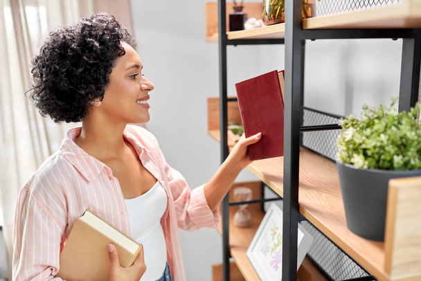 smiling woman arranging books on shelving at home - Foto, Imagen