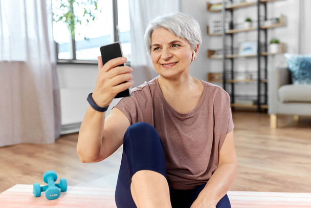woman with phone and earphones exercising at home - Foto, afbeelding
