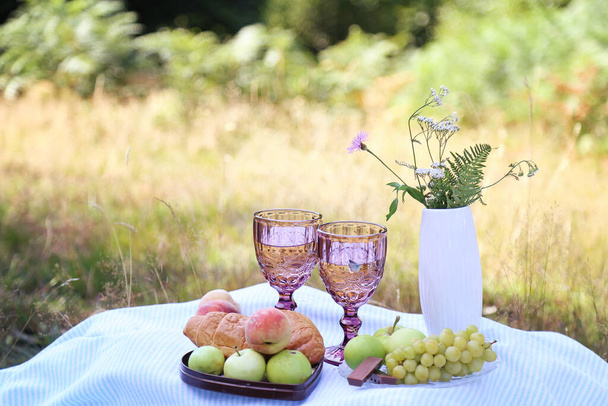 Summer picnic with croissants, fruits, chocolate and glasses of wine in the forest. Cottage core aesthetic. Summer vibe. Copy space - Foto, Imagem