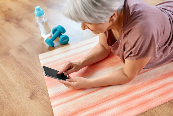 senior woman with smartphone exercising at home - Zdjęcie, obraz