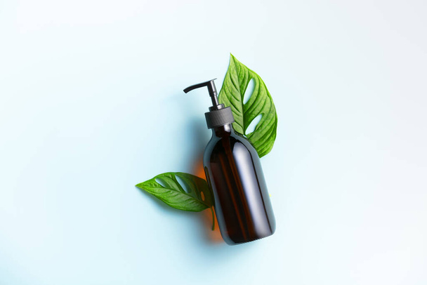 Banner. One cosmetic dark amber glass bottle with green plant on blue background - Fotografie, Obrázek