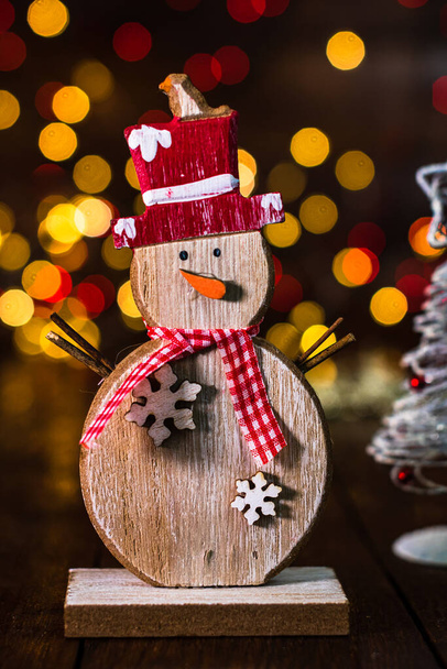 Weihnachtsdekoration vor verschwommenem Hintergrund und unscharfem Licht. Dekorativer Schneemann aus Holz und glitzernde Weihnachtskugeln - Foto, Bild