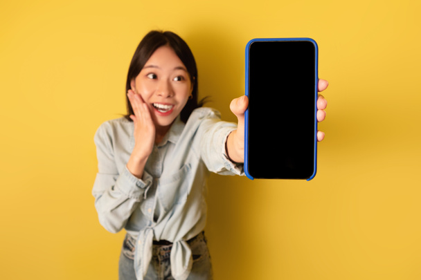 Excited millennial Asian lady presenting blank smartphone with mockup for mobile app or website design - Фото, изображение