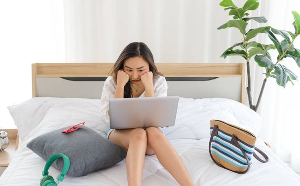 Młoda Azjatka emocjonalnie zdenerwowana, nieszczęśliwa lub smutna podczas pracy z laptopem na łóżku w domu - Zdjęcie, obraz