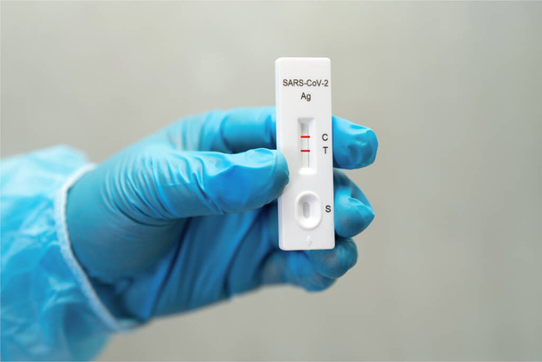 Médico asiático en traje PPE muestra resultado positivo de la prueba con el kit de prueba de antígeno de Saliva para comprobar el coronavirus Covid-19 en el hospital. - Foto, imagen