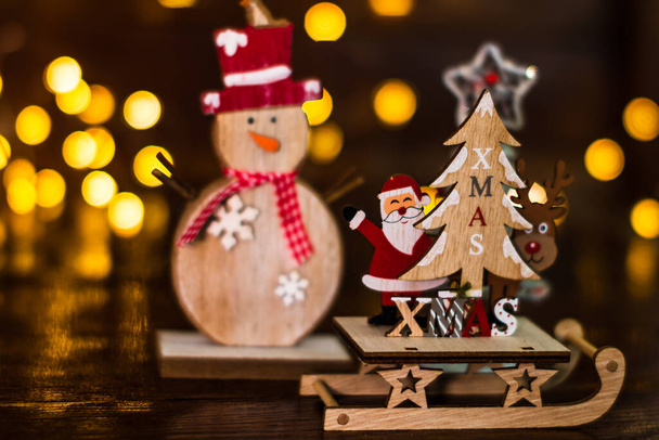 Dekoracje świąteczne na niewyraźnym tle. Zbliżenie drewniane sanie Boże Narodzenie z Santa Claus, renifer i choinka. - Zdjęcie, obraz