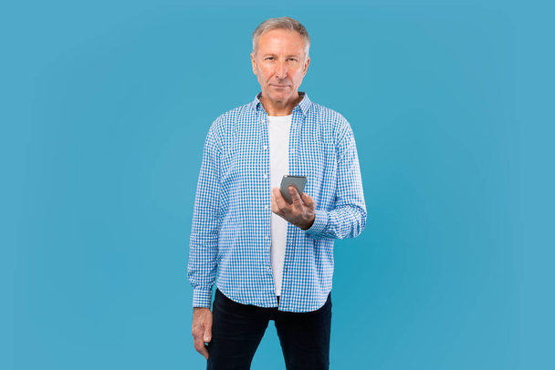 Mature man using his mobile phone at blue studio - Foto, afbeelding