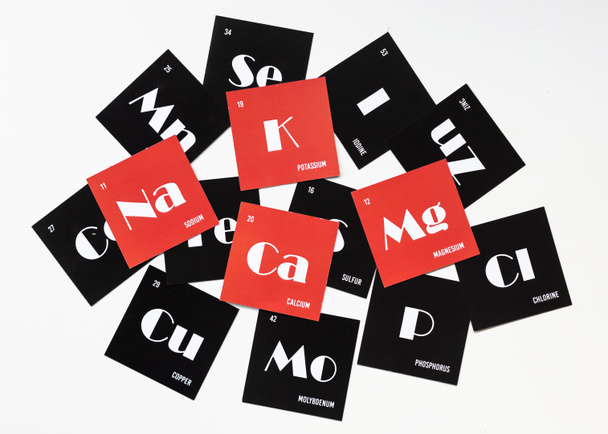 Tarjetas con los nombres de los elementos químicos del sistema periódico. Alfabeto de electrolitos sobre cartón rojo. Vista superior - Foto, imagen