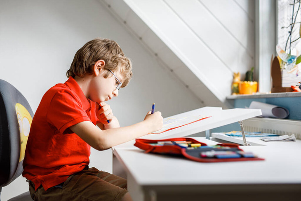 Portré a szemüveges kisfiúról, aki házi feladatot csinál, ír és tanul. Egy kisgyerek gyakorol a házban. Általános iskola és oktatás, otthoni oktatás koncepciója. - Fotó, kép