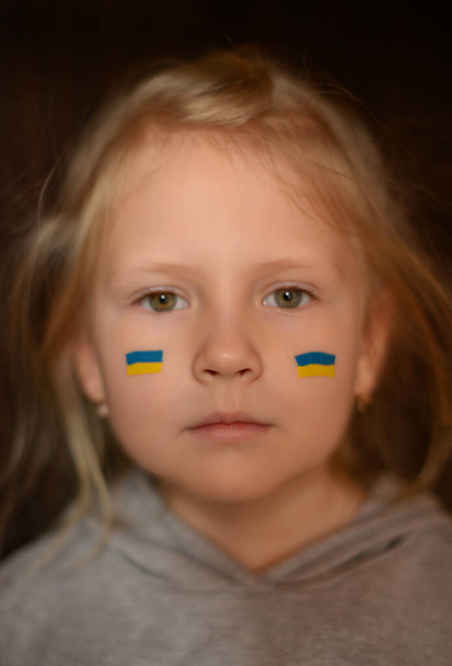 Sad Ukrainian child girl with a painted flag on his cheeks. Pray for Ukraine. - Foto, afbeelding