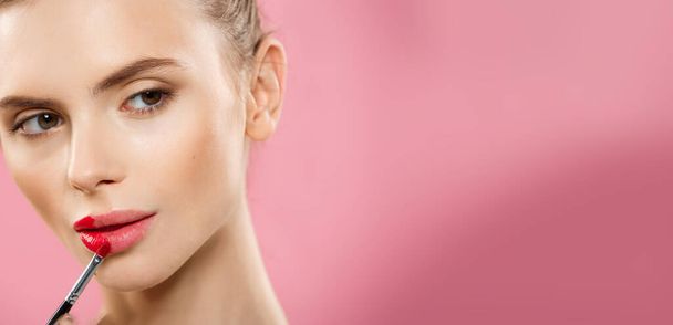 Concept Beauté - Femme appliquant rouge à lèvres rouge avec fond studio rose. Belle fille fait du maquillage
. - Photo, image
