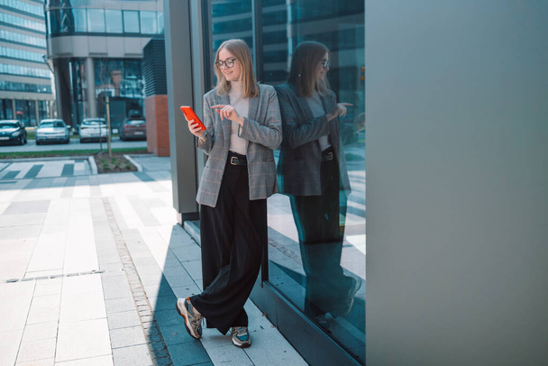 Donna d'affari creativa indossa vestiti alla moda digitando un messaggio di testo sul dispositivo smartphone vicino all'edificio per uffici loft - Foto, immagini