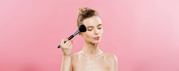 Beauty Concept - close-up mooie Kaukasische vrouw toepassing van make-up met cosmetische poeder borstel. Perfecte huid. Geïsoleerd op roze achtergrond en kopie ruimte. - Foto, afbeelding