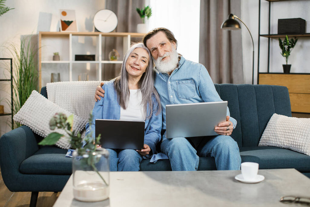Marido y esposa mayores sosteniendo una computadora portátil en sus vueltas y navegando por Internet juntos. - Foto, Imagen