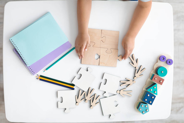 木製のパズルピースを保持する子供のトップビュー,教室でテーブルの上にジグソーパズルを接続する小さな手,フリースペース - 写真・画像