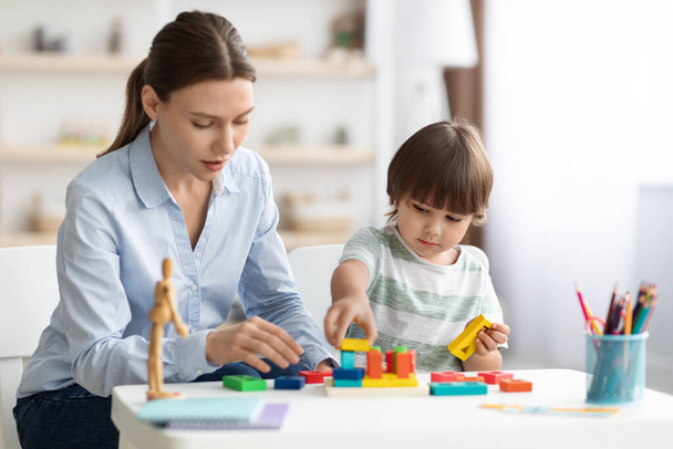 Cute little boy preschooler playing developing wooden games with professional woman psychologist at kindergarten - Photo, Image