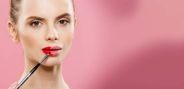 Beauty Concept - Woman applying red lipstick with pink studio background. Beautiful girl makes makeup. - Photo, Image