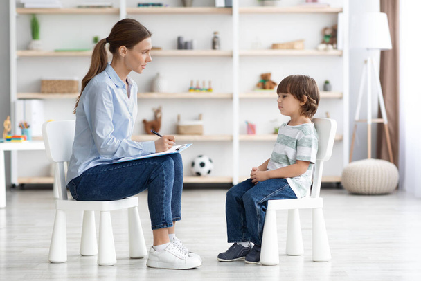 Ψυχολογική συμβουλευτική για παιδιά. Πλάγια εικόνα μιας επαγγελματία ψυχοθεραπεύτριας που κάθεται απέναντι στο αγοράκι - Φωτογραφία, εικόνα