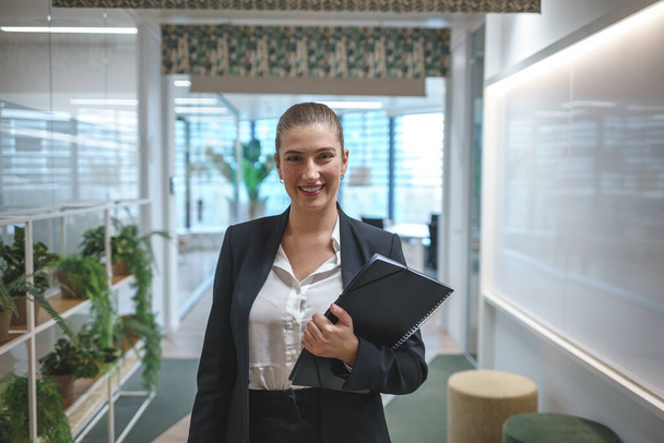 Cheerful businesswoman with folder in office hall - Fotoğraf, Görsel