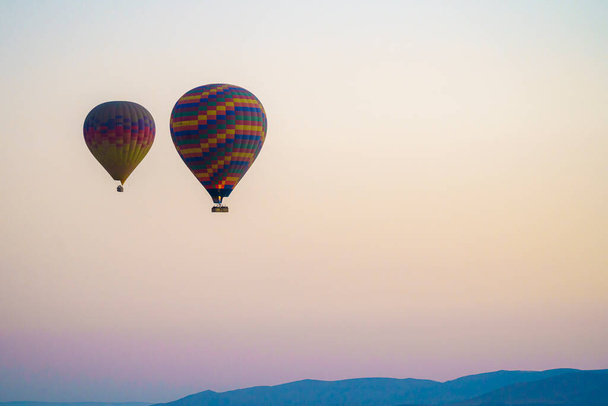 Balloons burning fuel as they fly over the city of Goreme with sightseeing tourists during a sunny summer day - 写真・画像