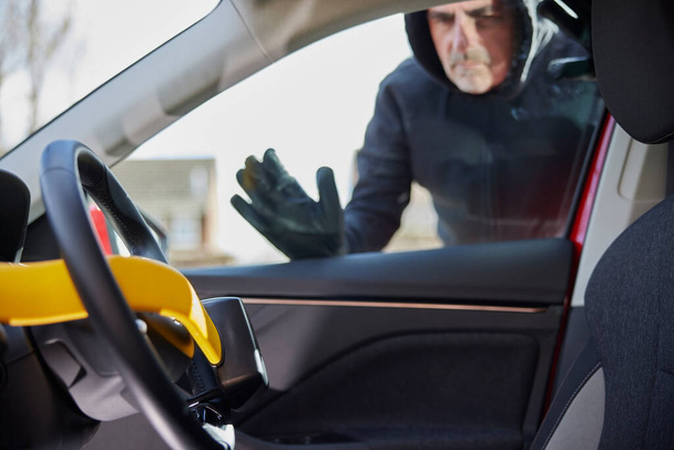 Männlicher Dieb blickt durch Fenster auf manuelle Lenkradverriegelung im Auto - Foto, Bild