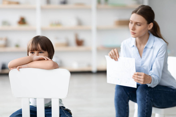 Inner mental problems. Stressed little boy sitting on chair and feeling upset, ignoring professional psychotherapist - 写真・画像